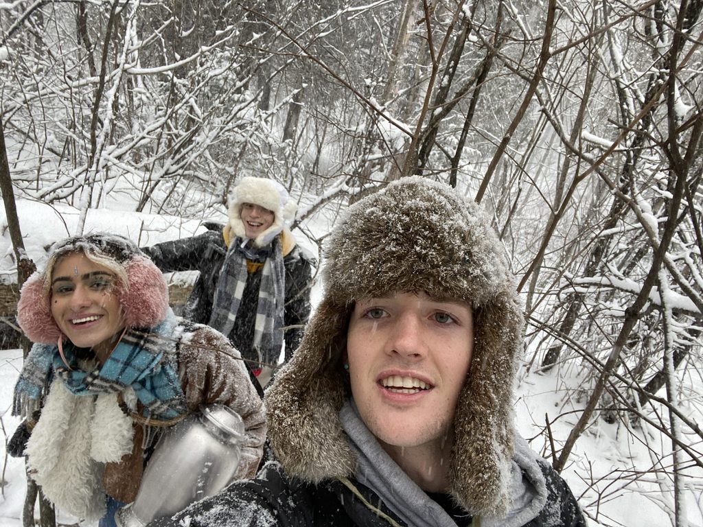 Three college students smile for the camera while standing in the snowy woods