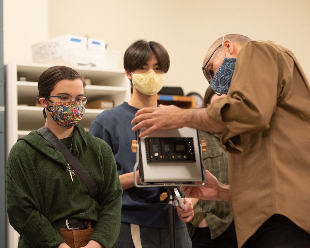 Two college students watch a male college professor work on a camera.