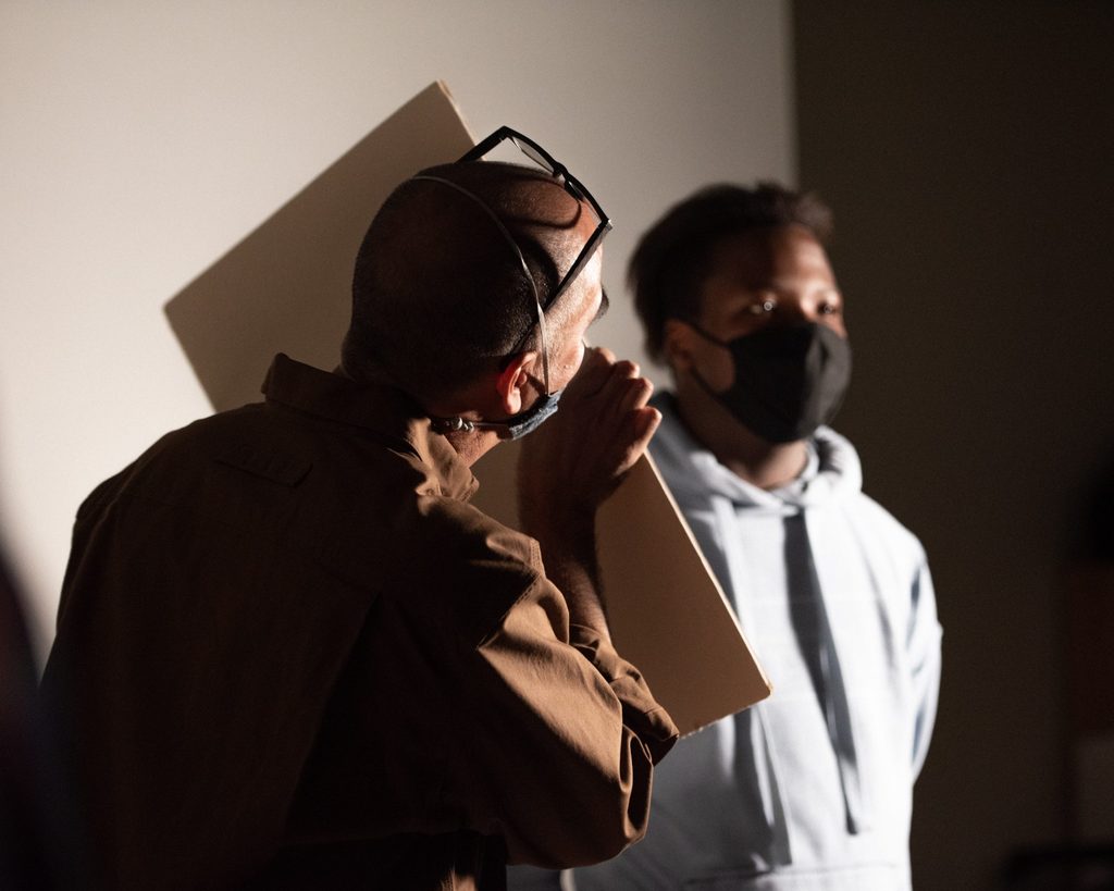 A professor holds a light reflector for a student being photographed.