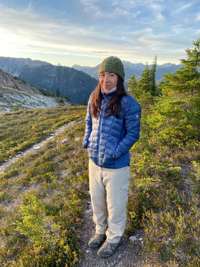 A woman stands in the wilderness.