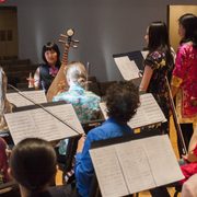 instructor teaching a musical instrument class with students, music stands and sheet music visible