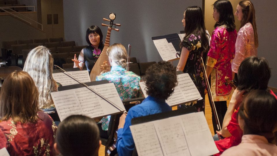 instructor teaching a musical instrument class with students, music stands and sheet music visible