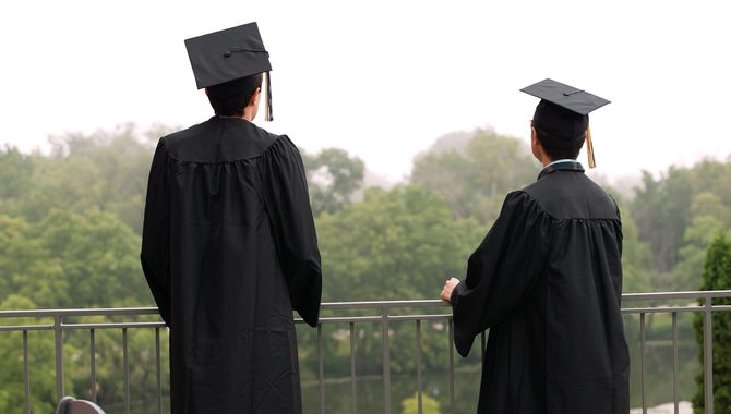 Two students in caps and gowns look out over campus from the Boliou Patio. Photo taken from behind the students.