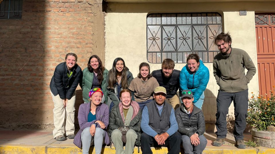 11 people, some students and some professors and mentors, pose for a group photo outside a building.