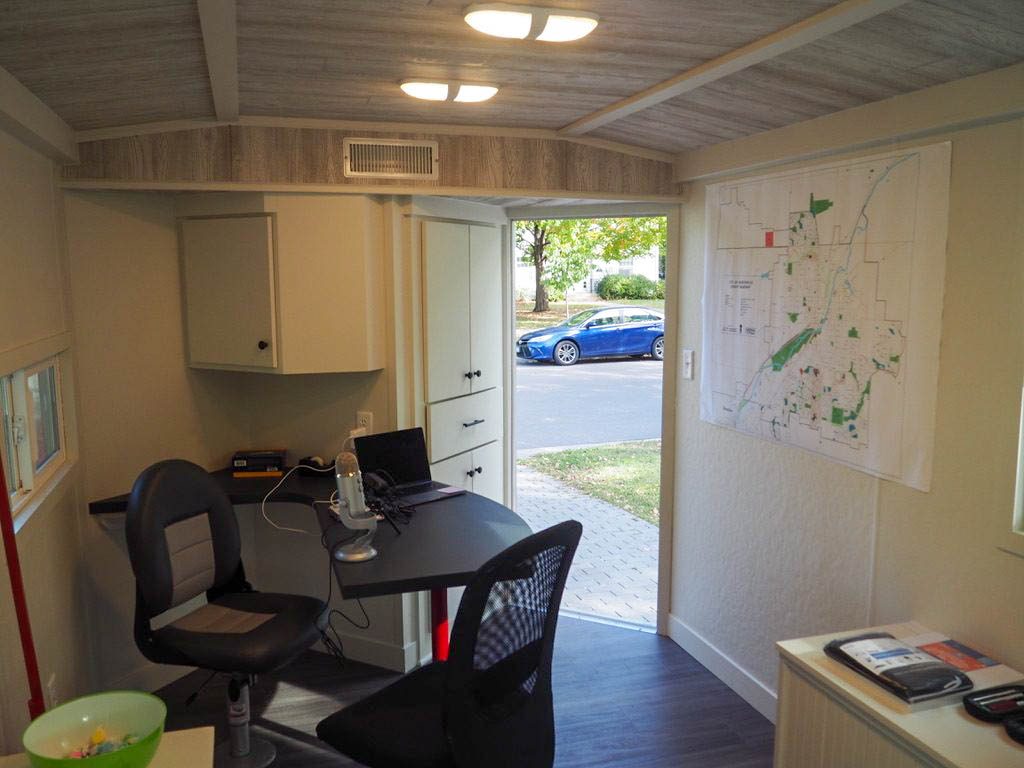 Photo taken from inside the Carleton Humanities and Arts Trailer. A desk with a microphone and laptop is the main focus, and a map of Northfield is pinned to the wall.