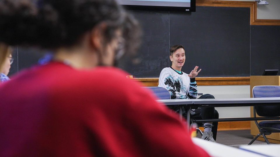 Shot taken from behind a student's shoulder of Phil Chan '06 teaching at the front of a classroom.
