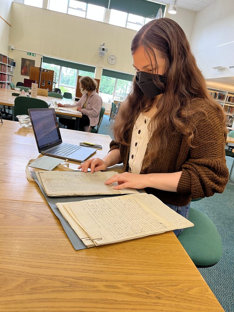 In a library, Margaret De Fer ’24 looks at old documents in a folder.