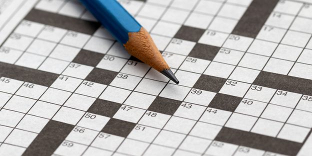 Close up of a blue pencil laying across a blank crossword puzzle.