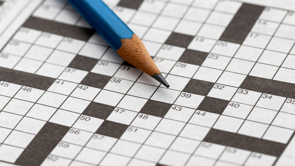 Close up of a blue pencil laying across a blank crossword puzzle.