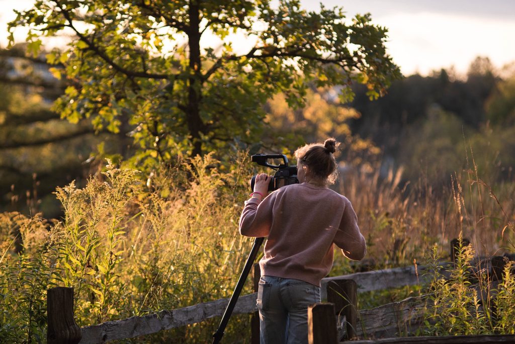 A student looks through a video camera on a tripod, observing the Arb during sunset.