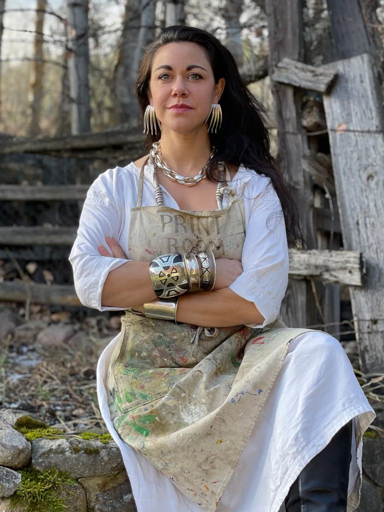 Ariana Boussard-Reifel poses in the woods in a paint-stained apron.