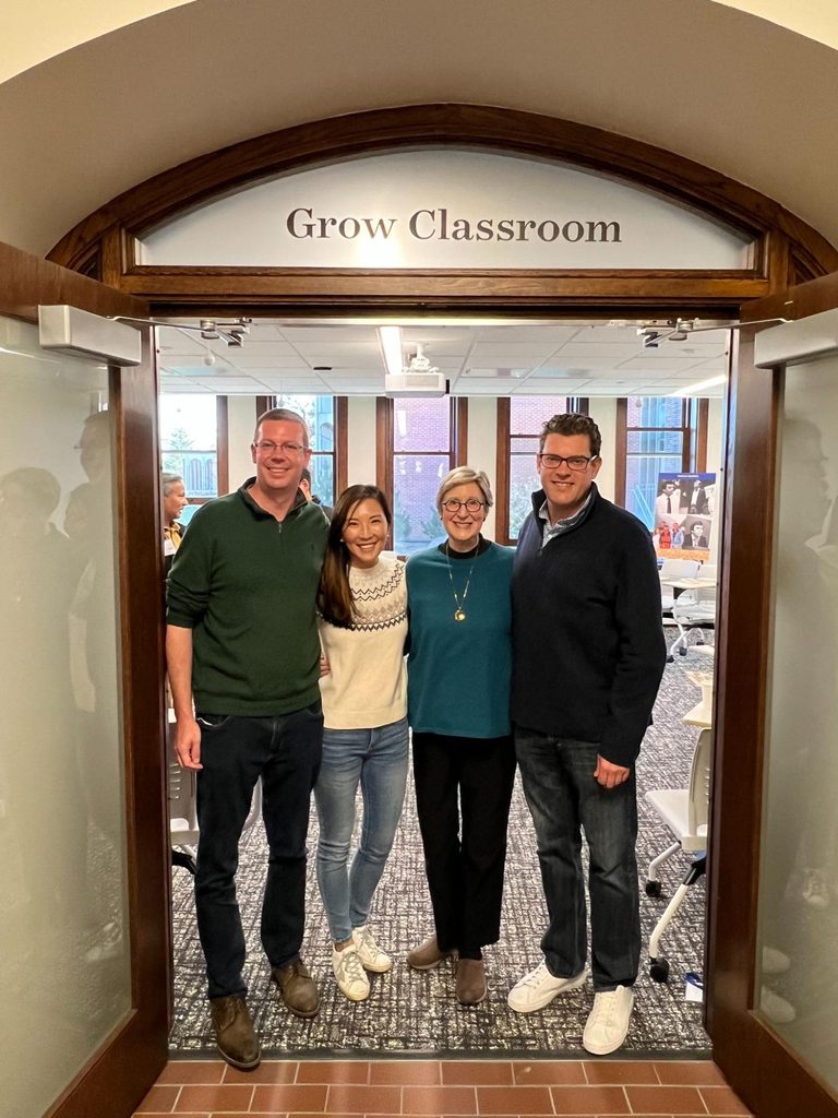 Lewis Grow, Mary Ann Hasenstab, Mary Lewis Grow and Michael Hasenstab smile at the camera from the doorway to the Grow Classroom, which is labeled with its name.