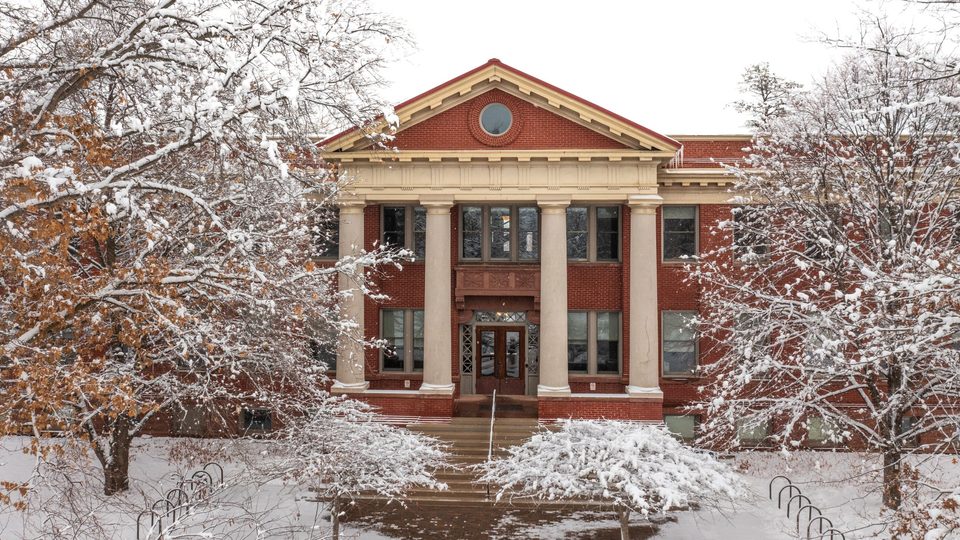 Wide shot of the front of Laird under a white sky, surrounded by snow-covered trees.