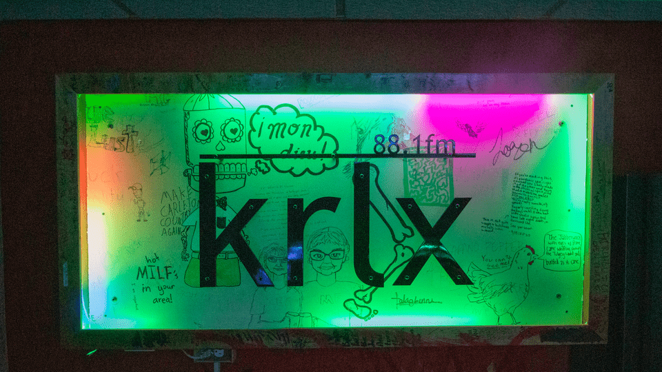 The KRLX radio sign, lit by colored lights and decorated with student doodles.