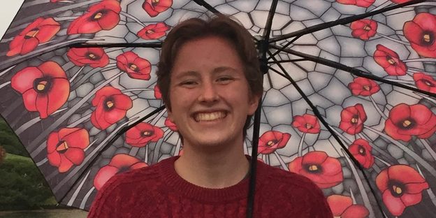 A student smiles in the rain under a floral umbrella.