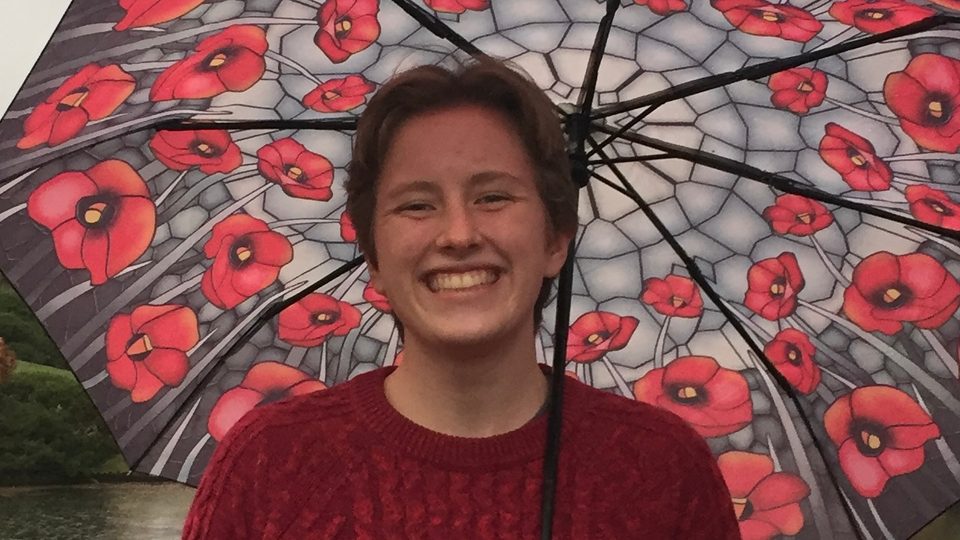 A student smiles in the rain under a floral umbrella.