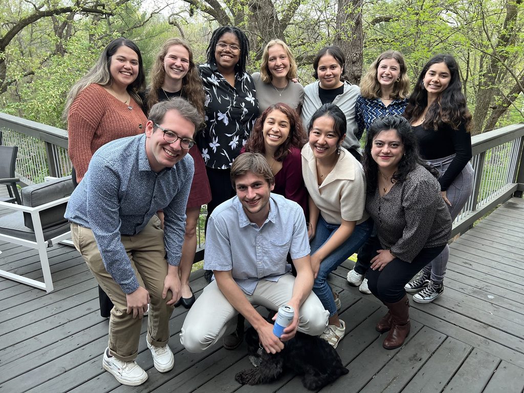A large group of students pose together on a wooden deck outside.