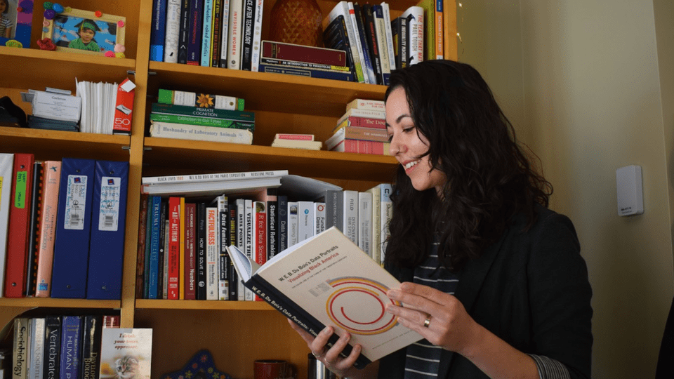 Lin Winton reads a book next to a full bookshelf.