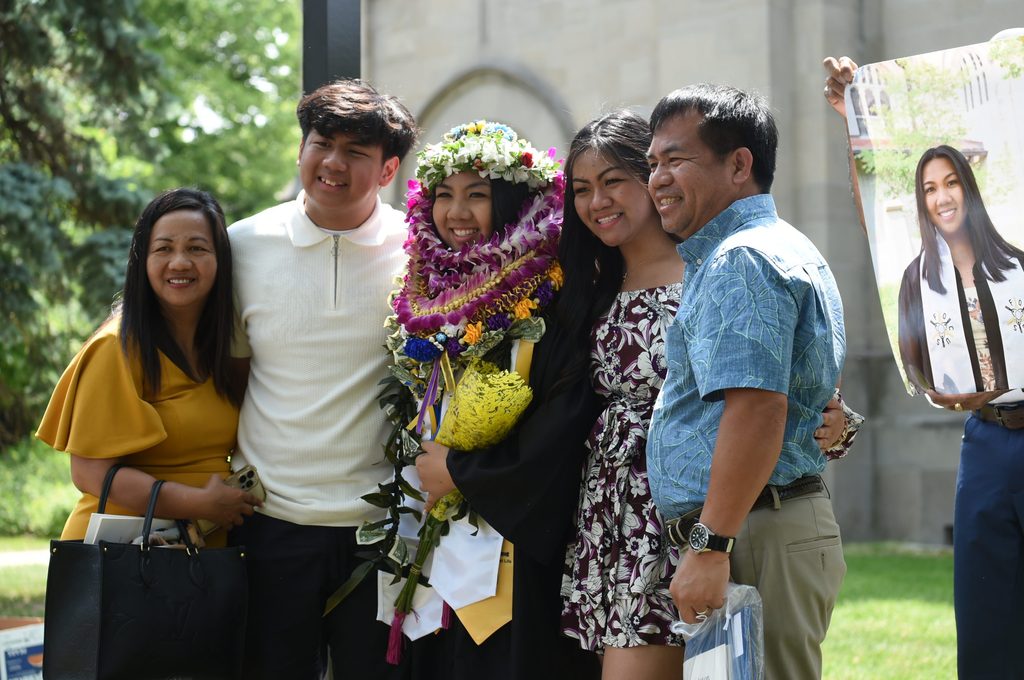 A student covered in leis and flowers poses with their family outside the Chapel.