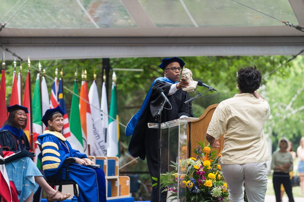 Jonathan Capehart ’89 hands off a Schiller bust to a student running across the stage at Commencement.