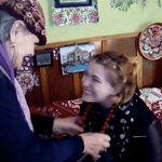 An older woman places a necklace on a student