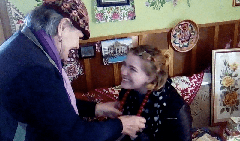 An older woman places a necklace on a student