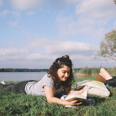 Student lying down reading nearby a river