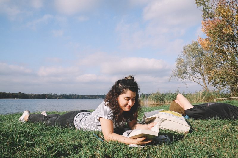 Student lying down reading nearby a river