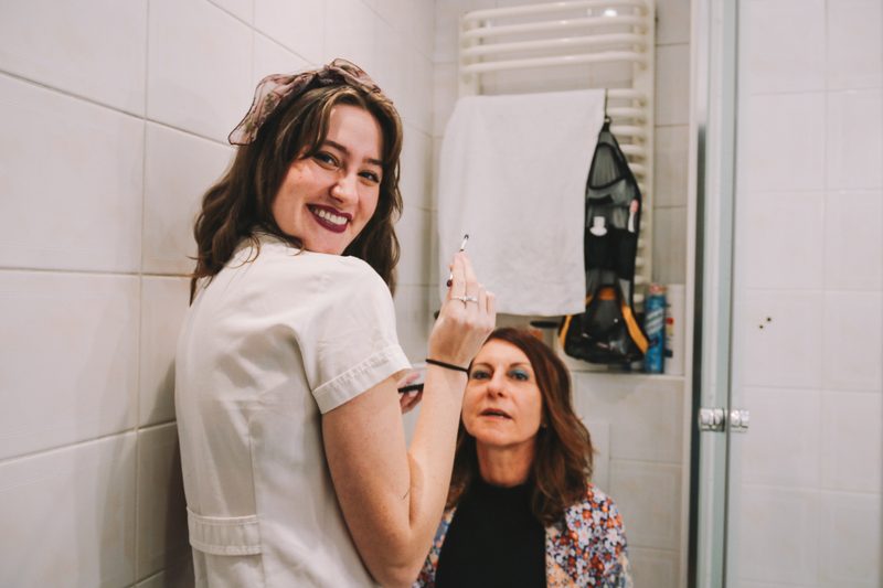 Student applying makeup to professor's face in the bathroom