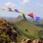 A man waves a string of bright cloth fabric in the wind on a mountain peak