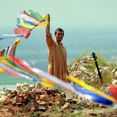 A man smiles while lifting a clothesline of bright cloth pieces