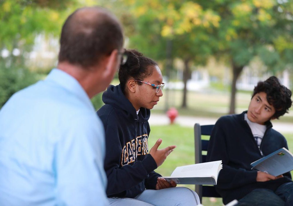 Student wearing Carleton sweatshirt reads aloud during outdoor class.