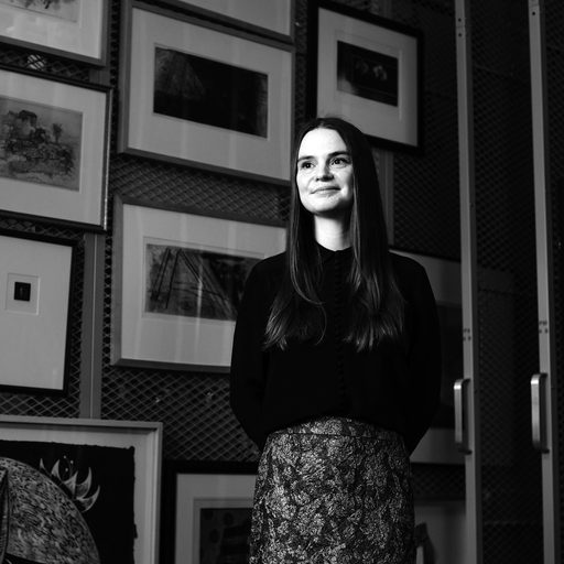 A woman with long hair stands in front of a wall of framed prints