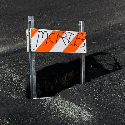 A big pothole in black concrete containing a traffic barricade that has 