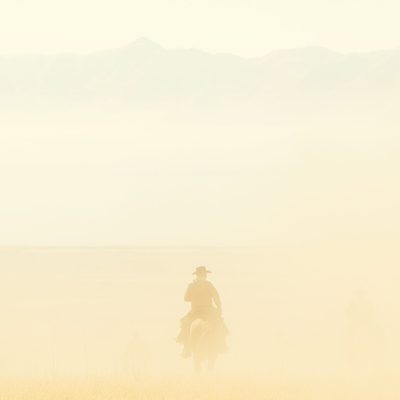 A cowboy riding off in the sunset through a cloud of light yellow dust.)