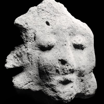 Black and white image of a rock shaped like a face with a mouth, nose, and closed eyes against a black background.]