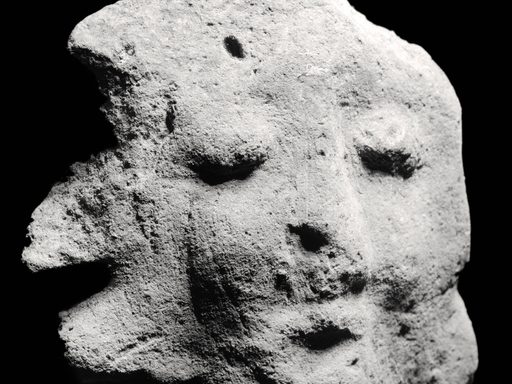 Black and white image of a rock shaped like a face with a mouth, nose, and closed eyes against a black background.]