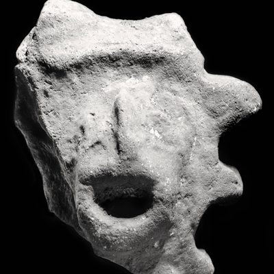 Black and white image of a rock shaped like a face with an open mouth against a black background.