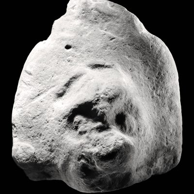 Black and white image of a rock shaped like a face with a large, protruding nose and sunken eyes against a black background.
