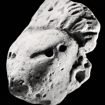 Black and white image of a rock shaped like a narrow face with long, straight hair against a black background