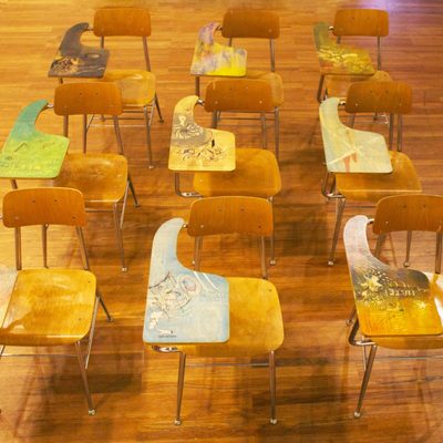 Image of wooden school desktops with art installations covering their desks in a variety of colors, from green to yellow to blue.