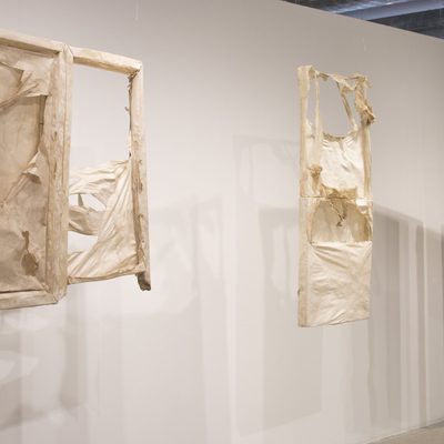 Hanging white rectangular frames filled with white paper that is torn in places.