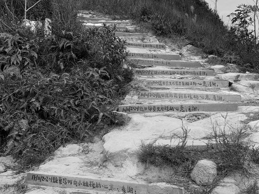 [Black and white photo of a trail towards the mountain; Chinese sentences painted on the steps indicating people who maintained the path.