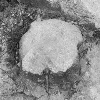 Black and white close up of a rock held in place by one piece of nail
