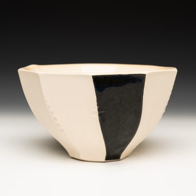 A faceted and textured bowl that is mostly white. One of the facets is glazed black.