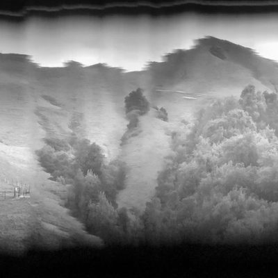 A long horizontal, black and white image of a hilly landscape has a rounded black border and some digital glitches that distort the panorama.