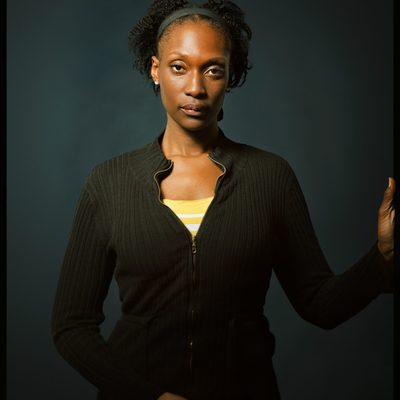 A Black woman looks at the camera and holds on to the edge of the frame with one hand with her cell phone in the other.