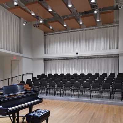 Photo of Applebaum Recital Hall, a choir rehearsal space, with piano, risers, and chairs.