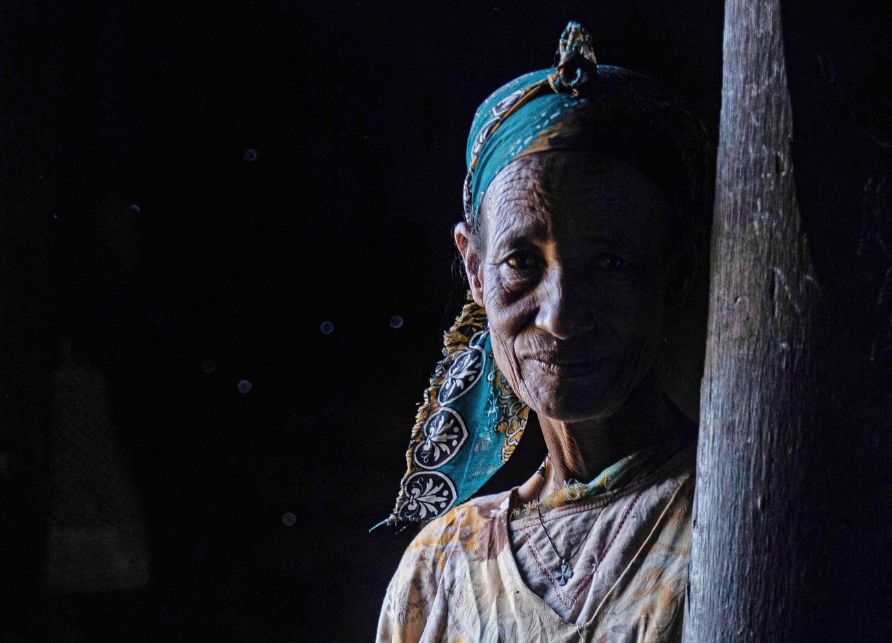 An Ethiopian woman in traditional clothing and a head scarf stands in a shadow