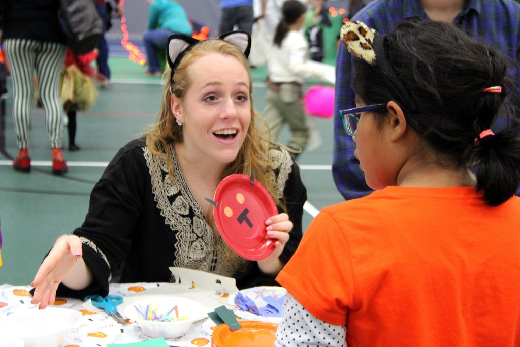 A student helps a child with crafts during Halloween Knights Carnival